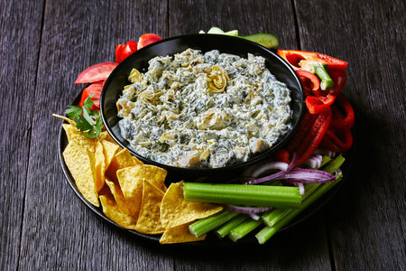 close-up of Spinach Artichoke leafy cheese Dip in a bowl with Tortilla Chips, cucumber, celery...