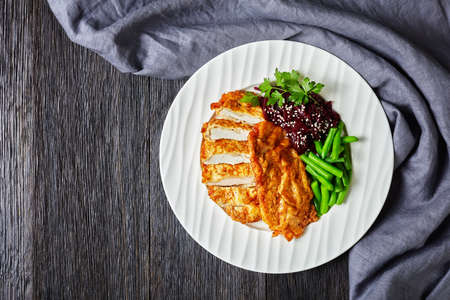 Chicken schnitzel served with beetroot salad and steamed crispy green bean on a white plate on a dark wooden table, horizontal view from above, flat lay, free spaceの写真素材
