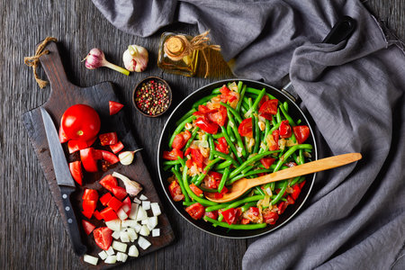 Caribbean stir-fried green beans with onions and tomatoes, Fry bodi in a skillet on a wooden table...
