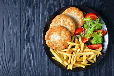 turkey burgers with lettuce tomato salad and chunky chips on a black plate on a wooden table, view from above, flatlay, free space for textの写真素材