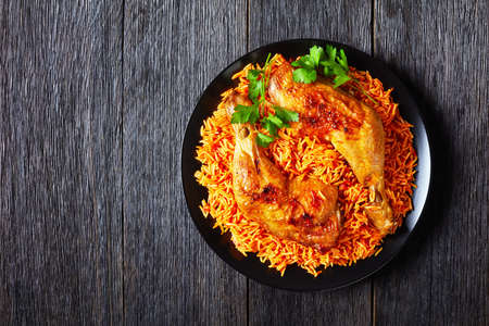 Roasted chicken legs with south indian long grain tomato rice cooked with sauteed tomatoes, onion, red chili powder, cinnamon, turmeric on a black plate, on rustic wooden background, copy spaceの写真素材