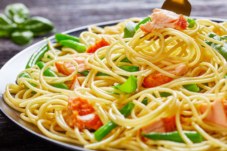Close-up of the fork with italian spaghetti, green bean, and salmon with fresh basil on top served on a black plate on a dark wooden backgroundの写真素材