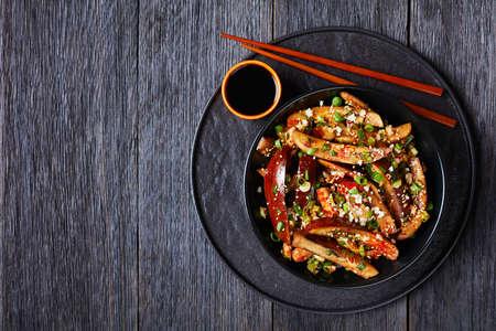 Gaji Namul, steamed and seasoned eggplant in a black bowl on a wooden table with soy sauce and chopsticks, korean side dish, landscape view from above, flat lay, free spaceの写真素材