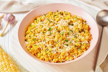 Parmesan Cilantro Corn in a pink bowl on a white wooden table with ingredients, landscape view from...