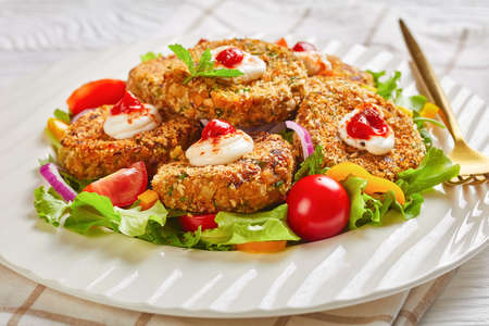 vegetarian burgers, patties of legume, onion and greens served on a white plate with fresh salad and tomato sauce, horizontal view from aboveの写真素材