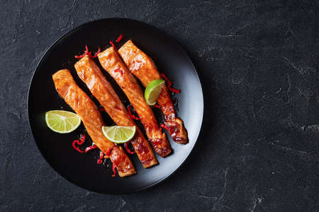 teriyaki salmon fillet baked in an oven served on a black plate with lime wedges on a concrete table, horizontal view from above, flat lay, free spaceの写真素材