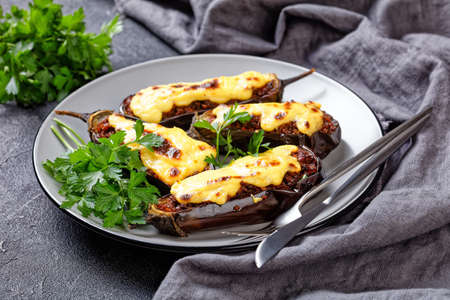 Greek stuffed eggplants with ground beef, tomatoes, topped with bechamel sauce with cheese, served on a plate with parsley on dark concrete background, top view, close-upの写真素材