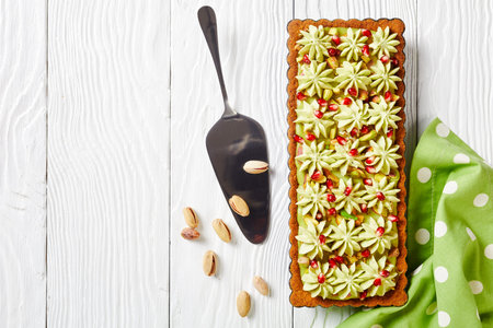 Pistachio ganache tart with pomegranate seeds on a square baking tin made of shortcrust pastry and...