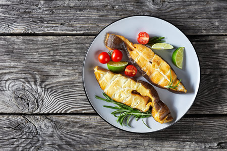 Traditional wild-caught smoked halibut fish steaks with lime, rosemary sprigs and tomatoes on a...
