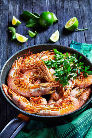 Garlic butter shrimps cooked on a skillet with lime and fresh parsley of big size shrimps or prawns served on a wooden background, top view, close-upの写真素材