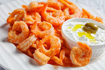 Seafood plate of fried garlic prawns or shrimps de shelled and de veined served with greek tzatziki sauce, green olives, rosemary on a white plate on a white wooden background, top view, close-upの写真素材