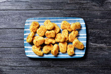 Easy fast food dish chicken nuggets of chicken breast pieces coated with breadcrumbs baked in the oven, served on a blue plate with rosemary and cutlery on a wooden background, top view, close-upの写真素材