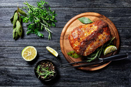 Sunday roasted pork tenderloin, juicy and succulent oven-baked piece of meat rubbed with mustard and spices: rosemary, bay leaf, lime juice, and pepper on a wooden background, close-up, top viewの写真素材