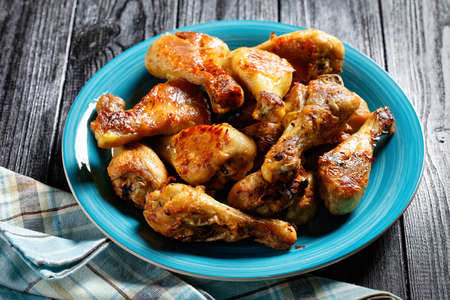Crispy baked chicken legs drumsticks served on a blue plate on a dark wooden background, top view, close-upの写真素材
