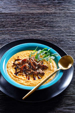Pumpkin soup of roasted pumpkin puree and wild mushrooms broth, topped with sesame seeds, vegan comfort dish, served on a blue plate with spoon and garlic on a dark wooden background, top viewの写真素材
