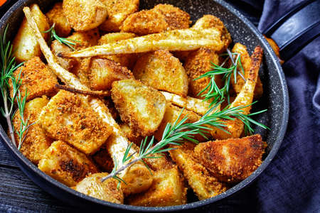 Oven baked root vegetables: parsnip and potato wedges breaded in breadcrumbs with smoked paprika and fresh rosemary sprigs served on a wooden background, top view, close-upの写真素材