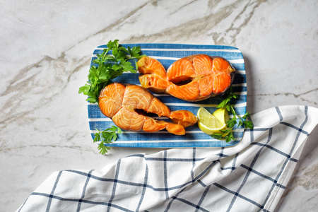 salmon steaks served with lemon wedges and parsley on a blue rectangular plate on a marble table, horizontal view from above, flat layの写真素材