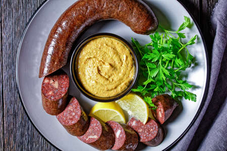 German blutwurst or german blood sausage sliced and served on a plate with parsley, mustard and lemon wedges served on a wooden table, top view, close-upの写真素材