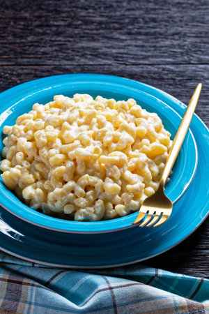 classic mac and cheese in a blue bowl with golden fork and napkin on a wooden table, vertical view...