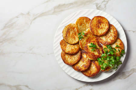 Potato pancakes with cottage cheese with garlic, parsley, served with sour cream dip on a plate on a light marble stone background with golden cutlery, top view, close-upの写真素材
