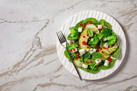 pear salad with blue cheese cubes, broccoli, spinach, dried cranberry and pomegranate seeds  on a plate on a marble table, flat lay, free space, horizontal view from aboveの写真素材