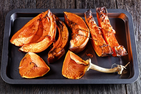 sliced butternut squash baked in an oven on a baking tray on a wooden table, horizontal view from aboveの写真素材