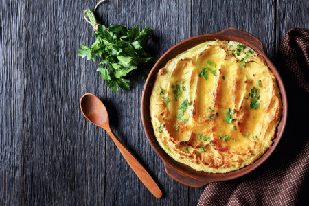 Garlic Parmesan Mashed Potato Casserole sprinkled with parsley in a dish on a dark wooden table, horizontal view from above, flat lay, free spaceの写真素材