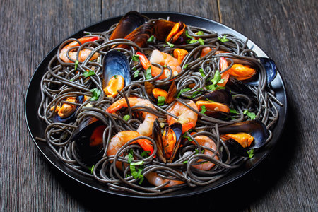 Squid ink pasta with seafood: mussels and shrimps on a black plate on a dark wooden background, top view, close-upの写真素材