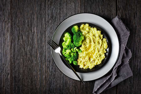 broccoli potato mash sprinkled with chopped almonds served with steamed broccoli florets on a black plate on a dark wooden table, horizontal view from above, flat layの写真素材