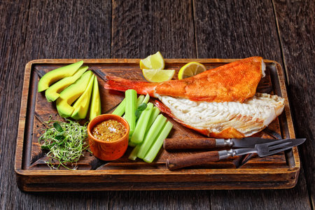 cold-smoked red snapper with celery sticks, lemon wedges, avocado slices and microgreens on a rude...