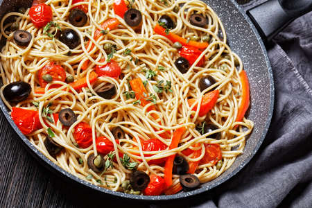 spaghetti alla caponata of whole-grain pasta with tomatoes, olives and capers in a skillet on a dark wooden tableの写真素材