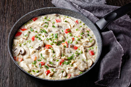 chicken a la king, cooked breast of chicken in a cream sauce with mushrooms, green peas and chopped peppers in a skillet on a dark wooden table, horizontal view from aboveの写真素材