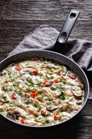 chicken a la king, cooked breast of chicken in a cream sauce with mushrooms, green peas and chopped peppers in a skillet on a dark wooden table, vertical view from aboveの写真素材