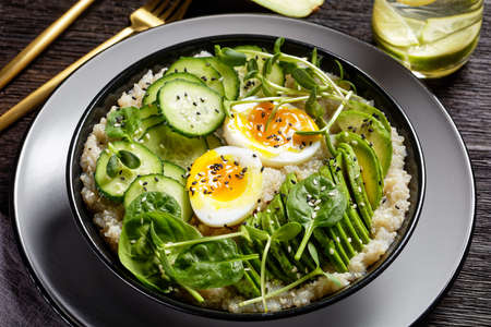 Egg Topped Quinoa Bowl with sunflower microgreens, cucumber, avocado, baby spinach in a black bowl on a dark wooden table, Turkish cuisineの写真素材