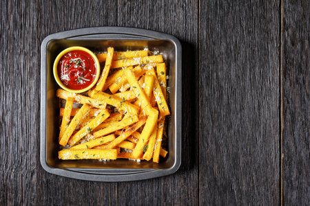 crispy baked polenta fries with parmesan cheese, thyme and spices in a baking dish with tomato sauce...