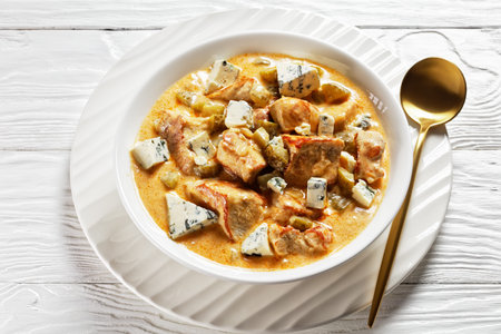 German cuisine: pork stew with cream, pickles, and blue mold cheese, smoked paprika served on a white plate with a golden spoon on white wooden background, top view, close-upの写真素材