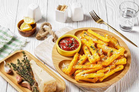 garlic parmesan polenta fries with parmesan cheese, thyme and spices in a bamboo dish with tomato sauce on a white wooden table, italy cuisineの写真素材