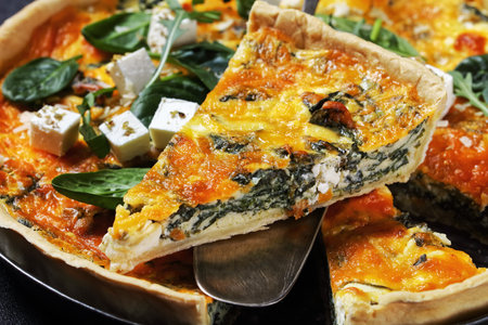 feta spinach cheddar cheese quiche in a baking dish on a wooden board on a grey concrete table with...