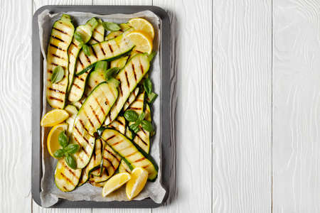 grilled zucchini slices on a sheet pan with lemon and fresh basil leaves, flat lay, free space, italian cuisineの写真素材