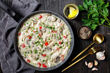 chicken a la king, cooked breast of chicken in a cream sauce with mushrooms, green peas and peppers in a saucepan on a wooden table, horizontal view from above, flat layの写真素材