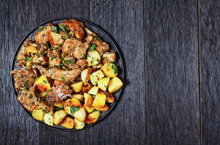 Conejo al ajillo, braised Rabbit with potatoes, garlic, white wine, salt, and olive oil on a black plate, spanish cuisine, flat lay, free spaceの写真素材