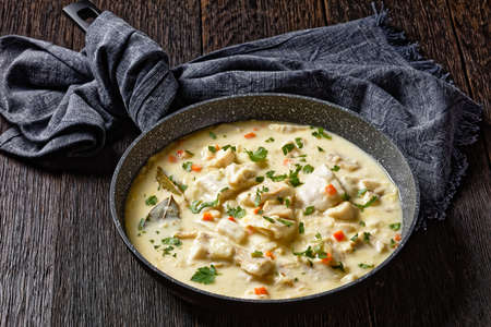 poached fish in milk base sauce with vegetables, spices and herbs in a pan on a wooden table, english cuisineの写真素材