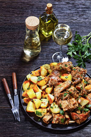 Conejo al ajillo, braised Rabbit with potatoes, garlic, white wine, salt, and olive oil on a black plate, spanish cuisine, vertical viewの写真素材