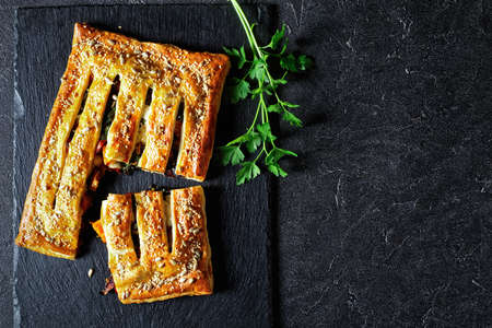 Puff pastry vegetable pie with goat cheese topped with roasted sunflower and sesame seeds filled with roasted vegetables: tomatoes, onion, and pumpkin, on a black slate, top view, close-upの写真素材