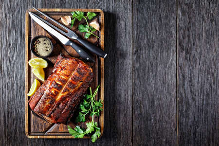 Barbecued Pork Loin Roast on a rude wooden cutting board with cutlery, horizontal view from above, flat lay, free spaceの写真素材