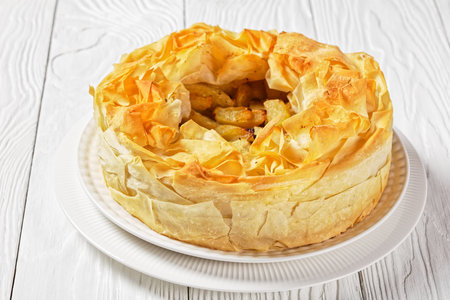 Layered Apple Pie With Phyllo Crust on a white platter on a white wooden table, horizontal view from...