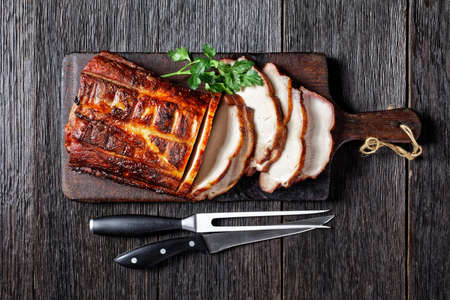 Barbecued Pork Loin Roast cut on slices on a rustic wooden cutting board with fork and knife, horizontal view from aboveの写真素材