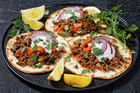 flatbreads topped with ground lamb, yogurt, coriander leaves and red onion on a black platter on a concrete table, top viewの写真素材