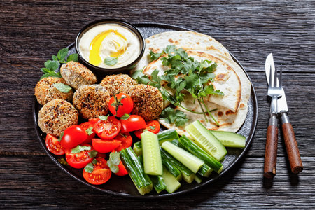 lamb meatballs served with flatbread, fresh cucumber, tomatoes and hummus on a black plate on a...