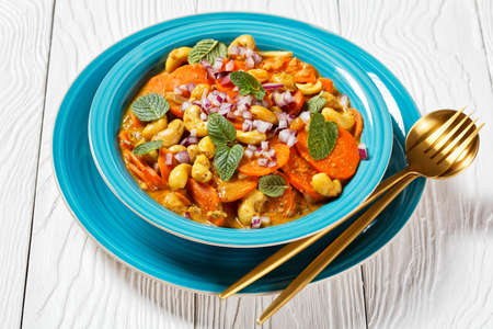 carrot curry with cashew and  raisins in a blue bowl on a white wooden table, horizontal view from above, indian cuisineの写真素材